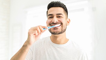 Man smiling while brushing his teeth