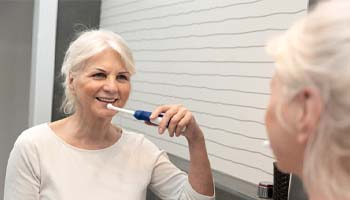 Older woman brushing her dental implants in Eatontown