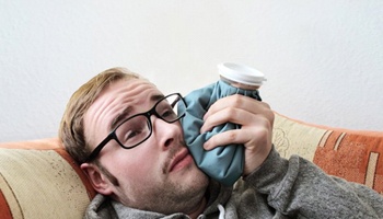 man lying on a couch and holding a cold compress to his cheek