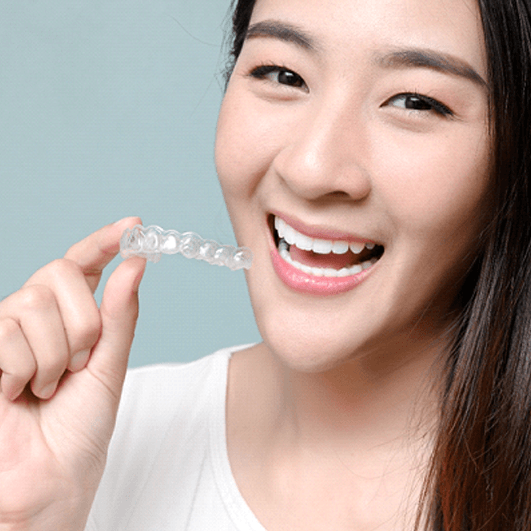 Portrait of smiling woman holding clear aligner close to her mouth