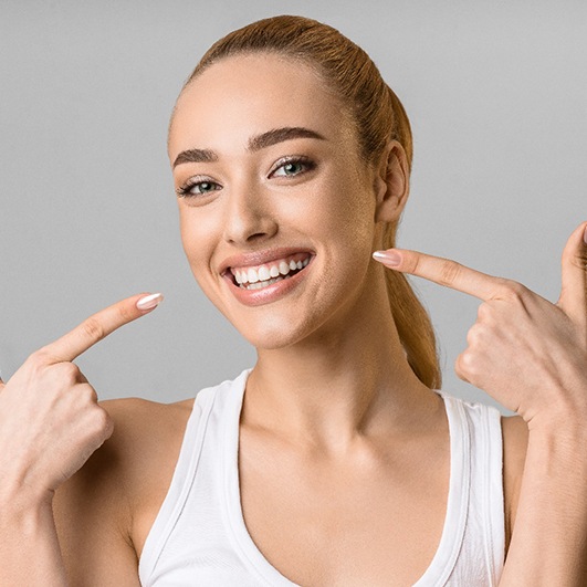 Woman pointing to her smile while wearing white tank top