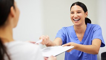 a person smiling while providing dental forms to a patient