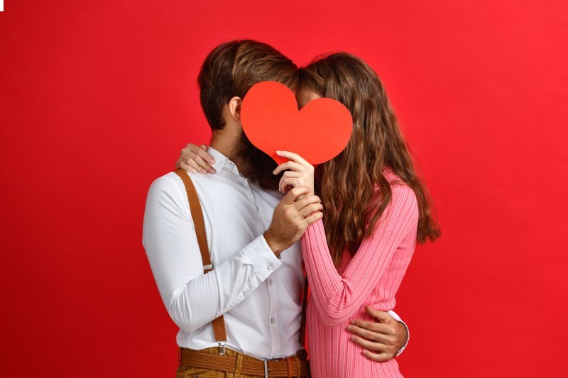 couple kissing behind paper heart