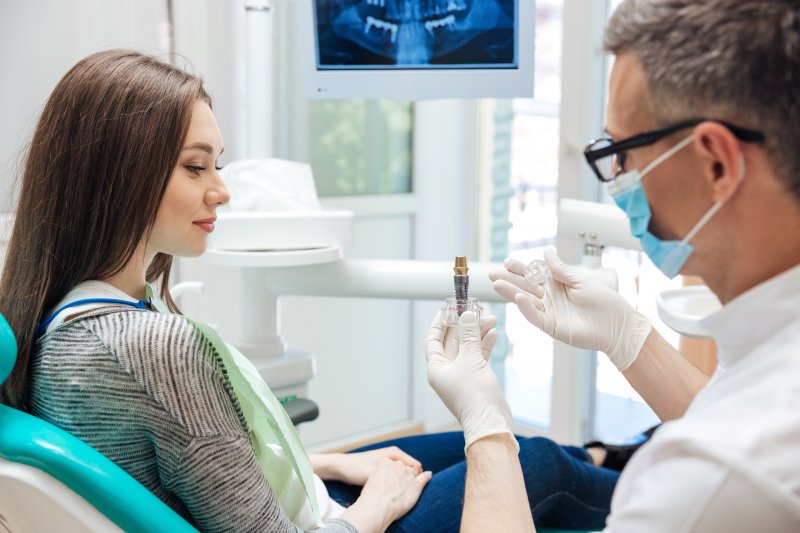 dentist showing their patient a model of a dental implant