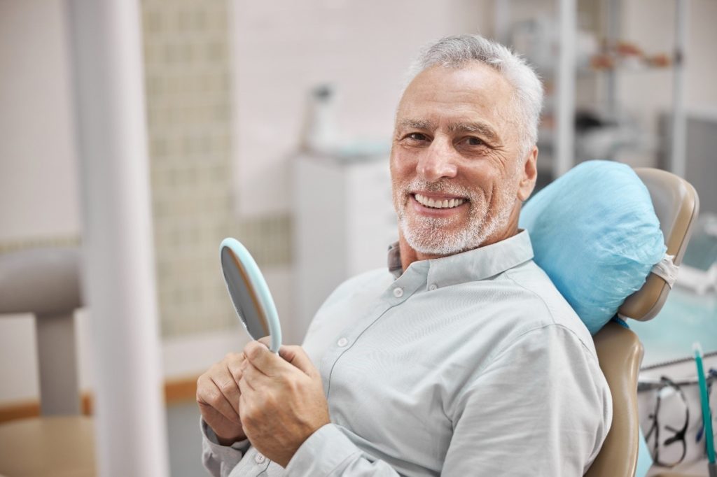 older man looking in the mirror at his teeth