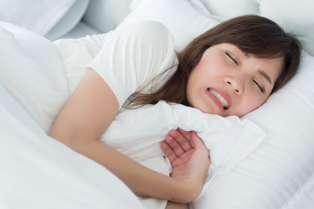 Woman asleep in white bedding clenching her teeth
